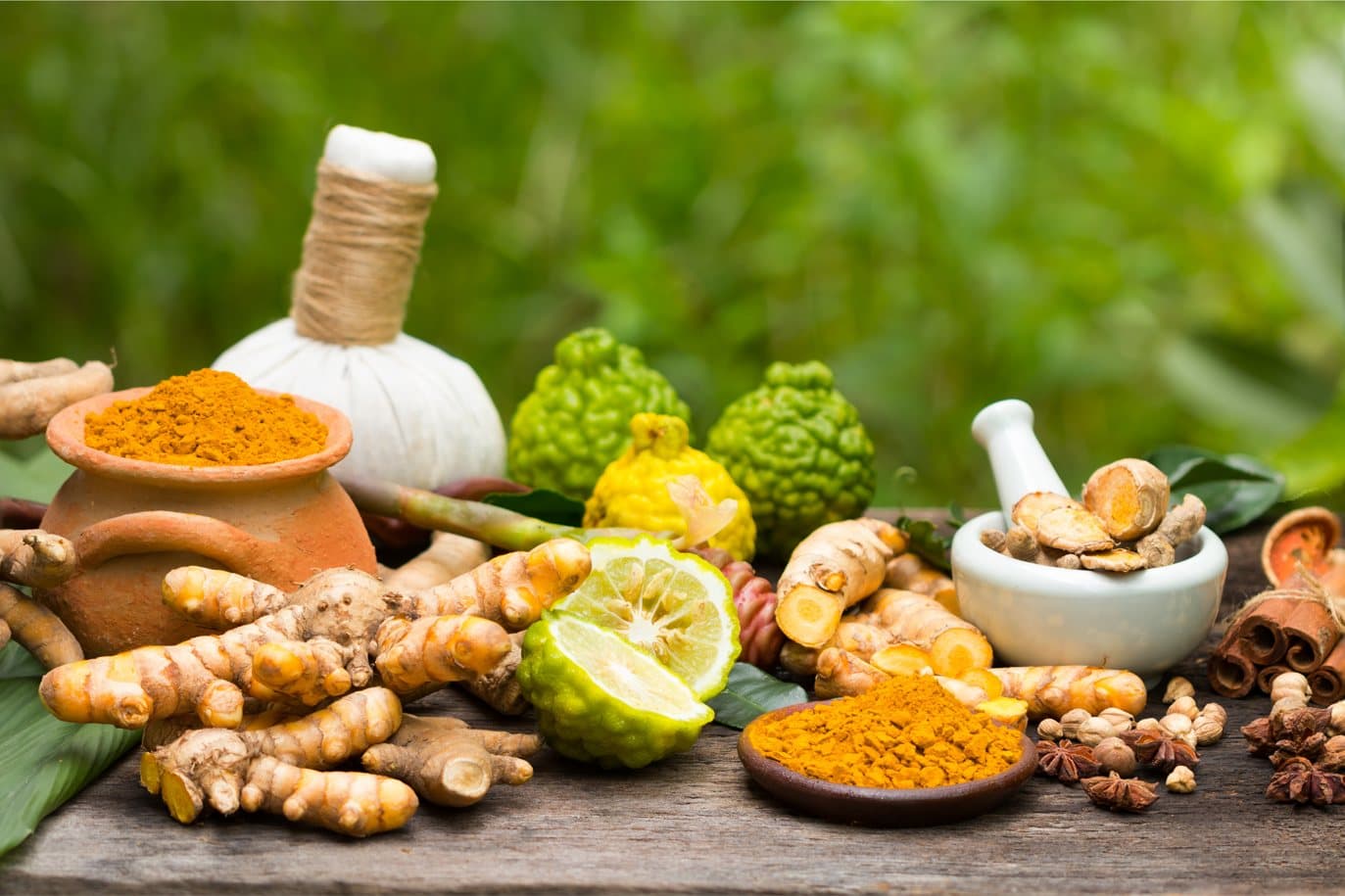 Fresh turmeric root, turmeric powder in a clay pot, a mortar and pestle, limes and spices on a wooden table.