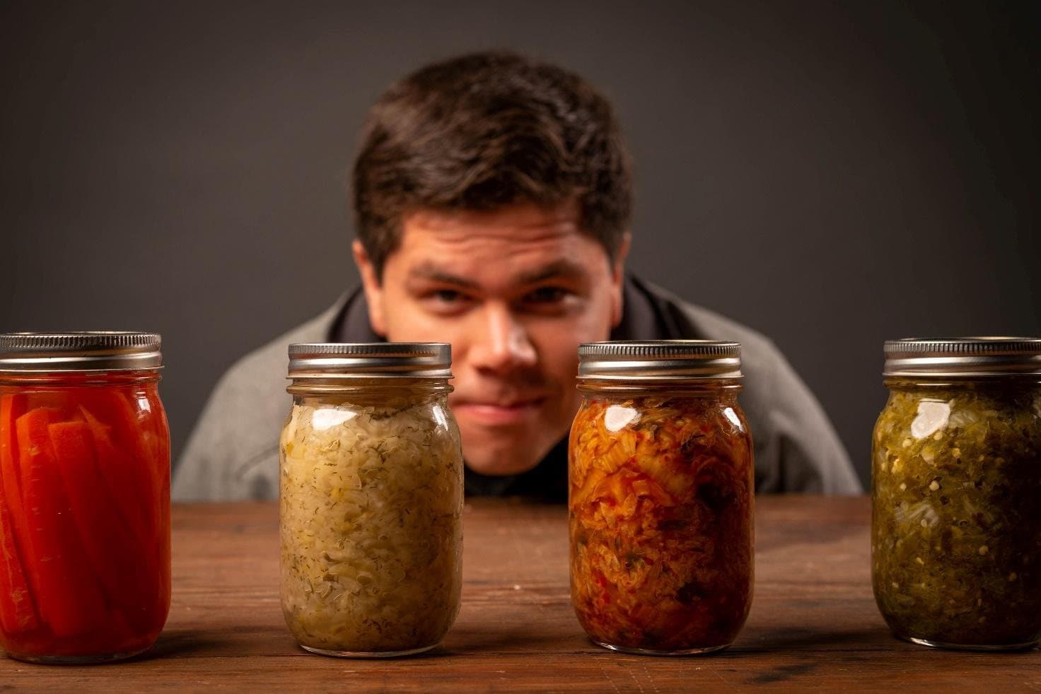 Four jars of fermented vegetables on a table with a person looking at them from behind.