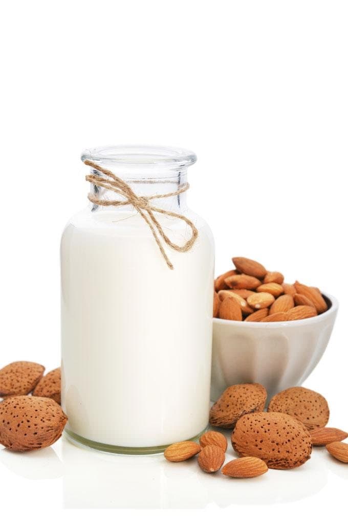A bottle of almond milk beside a bowl of almonds.