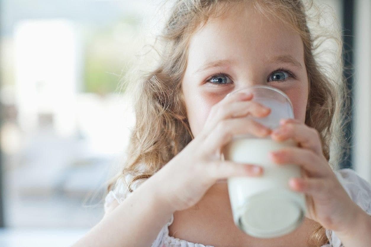 A young child drinking a glass of milk.
