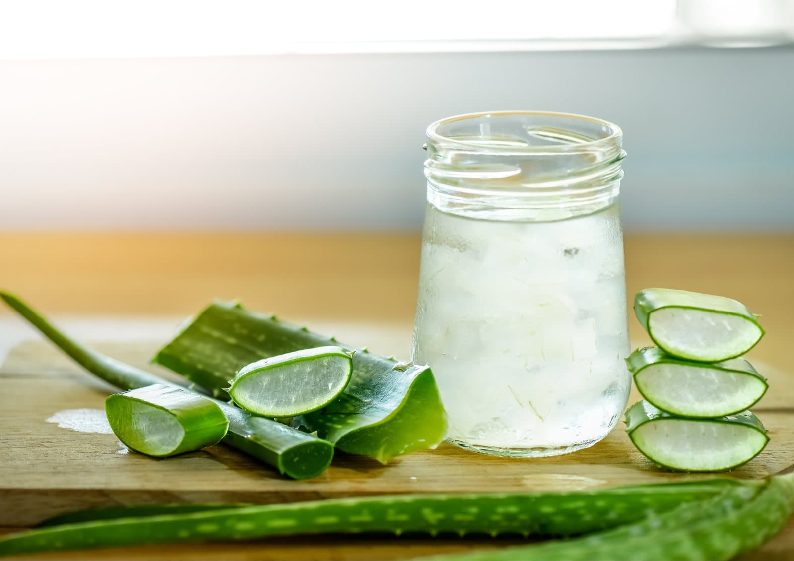 A jar of aloe vera juice beside sliced aloe vera leaves on a wooden board.