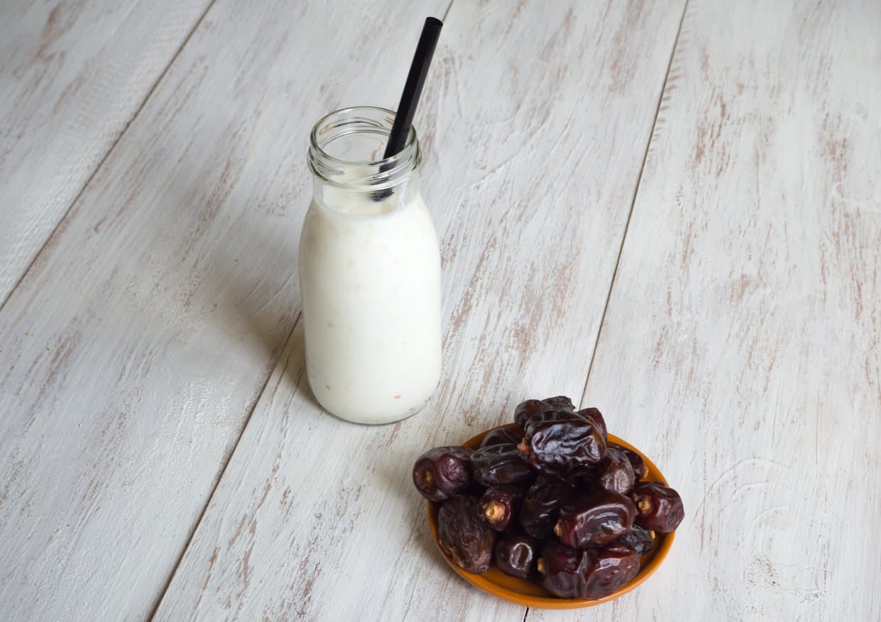 A bottle of yogurt smoothie with a straw beside a plate of dates.